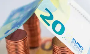 Stos monet euro i banknot 20 euro tworzą symboliczny dach nad domem.