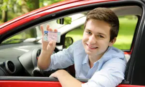 Uśmiechnięty młody mężczyzna w czerwonym samochodzie pokazuje prawo jazdy. Czy na prawo jazdy można wziąć kredyt na wymarzone auto?