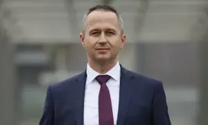 Mężczyzna w granatowym garniturze i bordowym krawacie, patrzący w obiektyw.