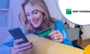 Uśmiechnięta kobieta z kartą płatniczą BNP Paribas w ręku korzysta z telefonu. Sprawdza BNP Paribas opłaty i prowizje.