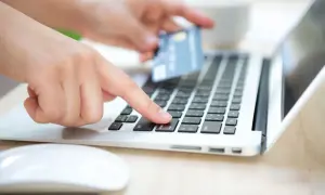 Dłoń z kartą zbliża się do klawiatury laptopa, by dokonać płatności. To może być rachunek rejestrowy PKO.