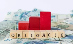 Drewniane klocki z napisem "OBLIGACJE" na tle polskich banknotów. Czy obligacje skarbowe są bezpieczne?