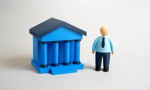 Figurka mężczyzny w niebieskiej koszuli i krawacie stoi obok niebieskiego budynku z kolumnami. Wibid on.
