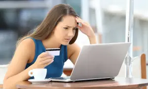 Zmartwiona kobieta z kartą płatniczą przed laptopem i filiżanką kawy.