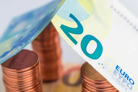 Stos monet euro i banknot 20 euro tworzą symboliczny dach nad domem.