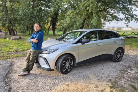 Mężczyzna opiera się o srebrny samochód, zastanawiając się, dlaczego nie warto kupować nowego samochodu.