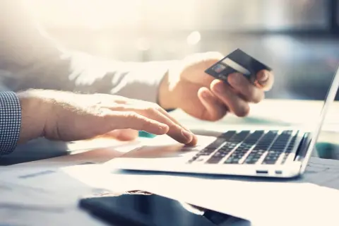 Dłoń trzyma kartę kredytową PKO, druga pisze na laptopie. Sprawdzam przejrzysta karta kredytowa PKO opłaty.