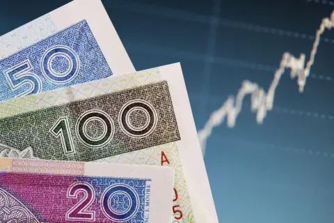 Polskie banknoty 50, 100 i 200 zł na tle wykresu giełdowego.