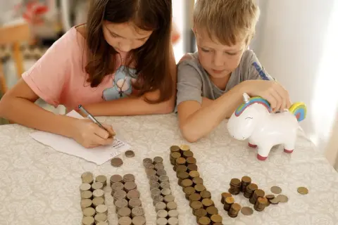 Dzieci liczą monety przy skarbonce w kształcie jednorożca. To świetny sposób na naukę oszczędzania, jak na nest bank konto dla dziecka.