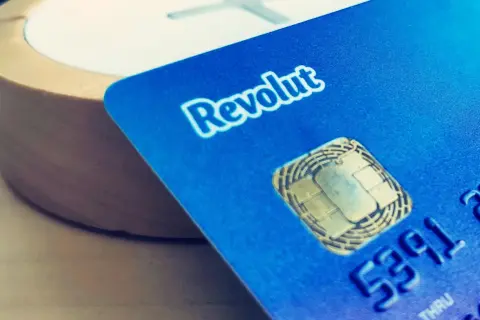 Niebieska karta Revolut z chipem i częścią numeru, na tle drewnianego przedmiotu.