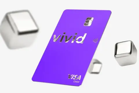 Fioletowa karta Vivid Visa Debit z błyszczącym logo, otoczona metalicznymi sześcianami. Wiele pozytywnych vivid money opinie potwierdza jej funkcjonalność.