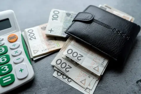 Portfel z polskimi banknotami i kalkulatorem. Rosnąca inflacja w Polsce sprawia, że pieniądze topnieją.