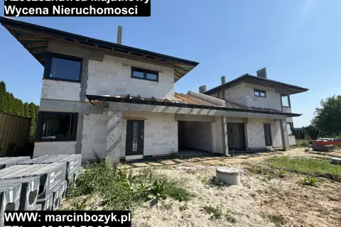 Budowa domu z białych pustaków, widoczne okna i dach. Na dole logo i dane kontaktowe.
