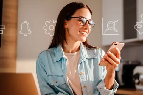 Uśmiechnięta kobieta w okularach trzyma smartfon, na tle ikony finansowe: wykres, dzwonek, koło zębate, lupa, skarbonka.