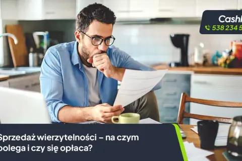 Mężczyzna w okularach analizuje dokumenty przy biurku, obok laptop i filiżanka.