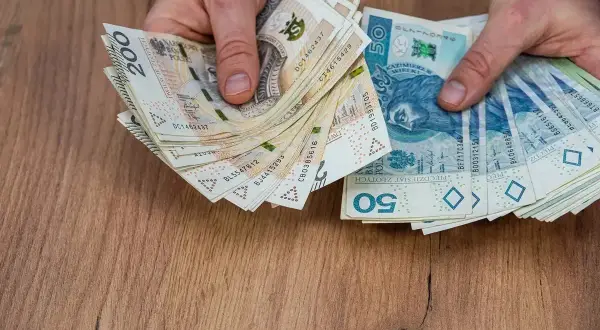 Dłonie trzymające stos polskich banknotów 50 zł i 200 zł na drewnianym tle.