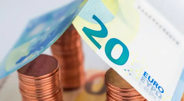 Stos monet euro i banknot 20 euro tworzą symboliczny dach nad domem.