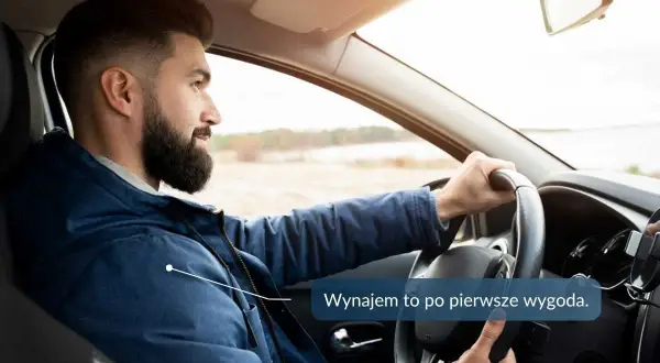 Mężczyzna z brodą prowadzi samochód, trzymając kierownicę.