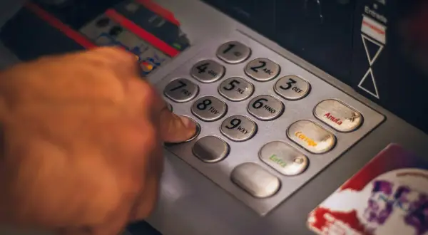 Dłoń wpisująca PIN na klawiaturze bankomatu.