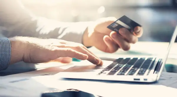 Dłoń trzyma kartę kredytową PKO, druga pisze na laptopie. Sprawdzam przejrzysta karta kredytowa PKO opłaty.