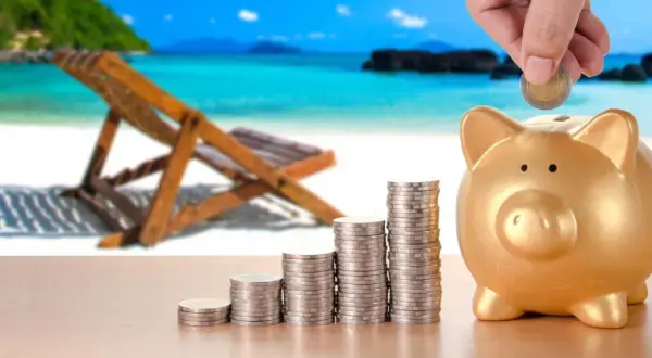 Złota świnka skarbonka i rosnące stosy monet na tle plaży. Marzysz o wakacjach? Otwórz konto oszczędnościowe bez konta osobistego i zacznij odkładać na podróż!