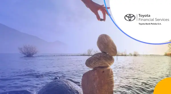 Równowaga kamieni na brzegu jeziora, ręka kładzie ostatni kamień. Logo Toyota Bank.