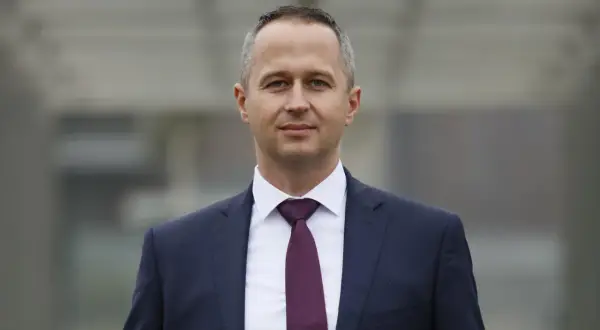 Mężczyzna w granatowym garniturze i bordowym krawacie, patrzący w obiektyw.