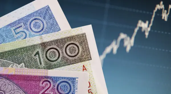 Polskie banknoty 50, 100 i 200 zł na tle wykresu giełdowego.