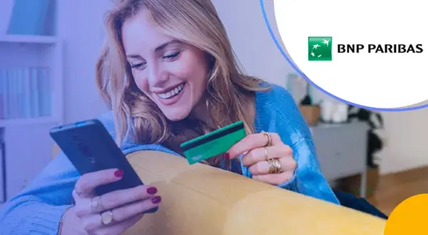 Uśmiechnięta kobieta z kartą płatniczą BNP Paribas w ręku korzysta z telefonu. Sprawdza BNP Paribas opłaty i prowizje.
