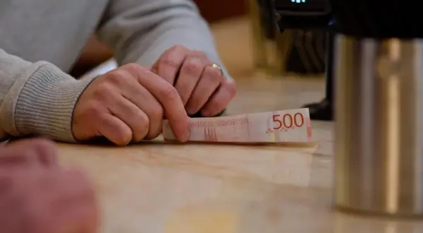 Dłoń trzyma banknot 500 koron szwedzkich. W tle terminal płatniczy. Tak jak obligacje można sprzedać przed terminem ich wykupu przez emitenta, tak i pieniądze można wydać.