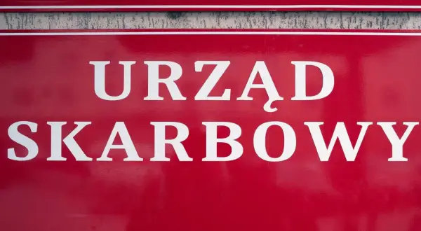 Czerwona tablica z białym napisem "URZĄD SKARBOWY". Współwłaściciel konta bankowego a urząd skarbowy - ważne sprawy podatkowe.