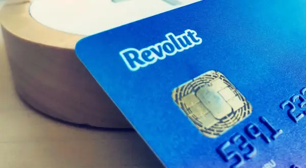 Niebieska karta Revolut z chipem i częścią numeru, na tle drewnianego przedmiotu.