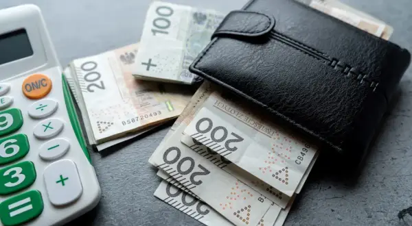 Portfel z polskimi banknotami i kalkulatorem. Rosnąca inflacja w Polsce sprawia, że pieniądze topnieją.