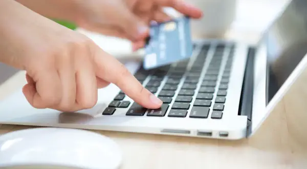 Dłoń z kartą zbliża się do klawiatury laptopa, by dokonać płatności. To może być rachunek rejestrowy PKO.