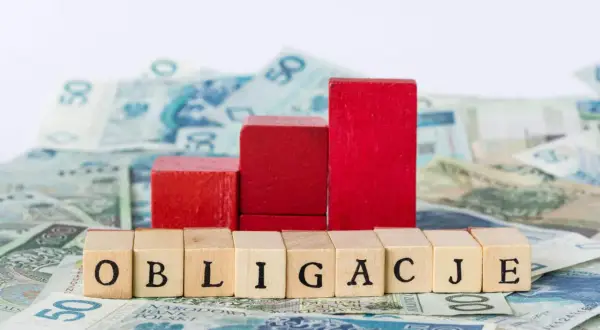 Drewniane klocki z napisem "OBLIGACJE" na tle polskich banknotów. Czy obligacje skarbowe są bezpieczne?