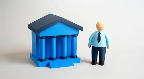 Figurka mężczyzny w niebieskiej koszuli i krawacie stoi obok niebieskiego budynku z kolumnami. Wibid on.