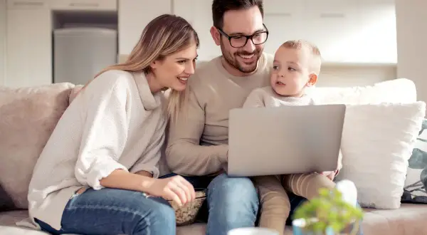 Rodzina z dzieckiem ogląda coś na laptopie, siedząc na kanapie.