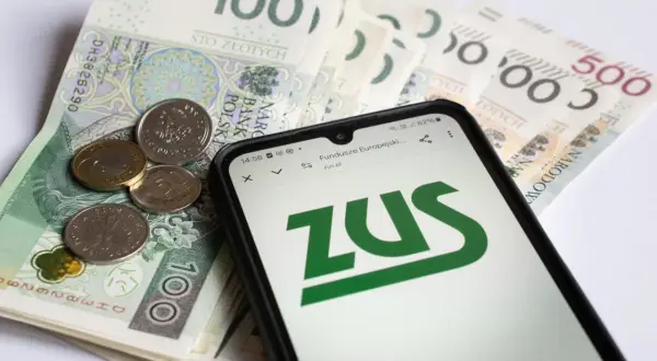 Złote banknoty i monety na nich leżący smartfon z logo ZUS.