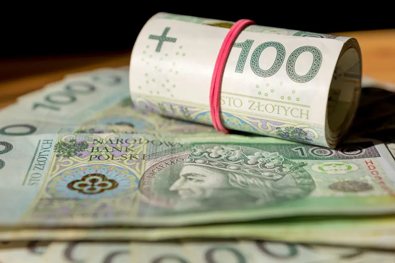 Zwijana rolka banknotów 100 zł, leżąca na stosie pieniędzy. Zastanawiasz się, w co zainwestować 20 tys.?