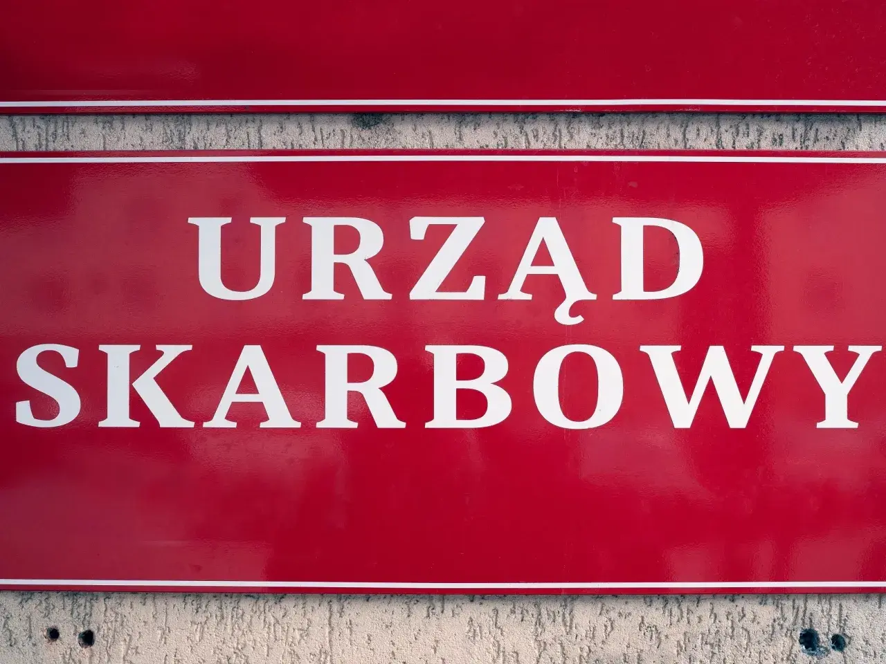Czerwona tablica z białym napisem "URZĄD SKARBOWY". Współwłaściciel konta bankowego a urząd skarbowy - ważne sprawy podatkowe.
