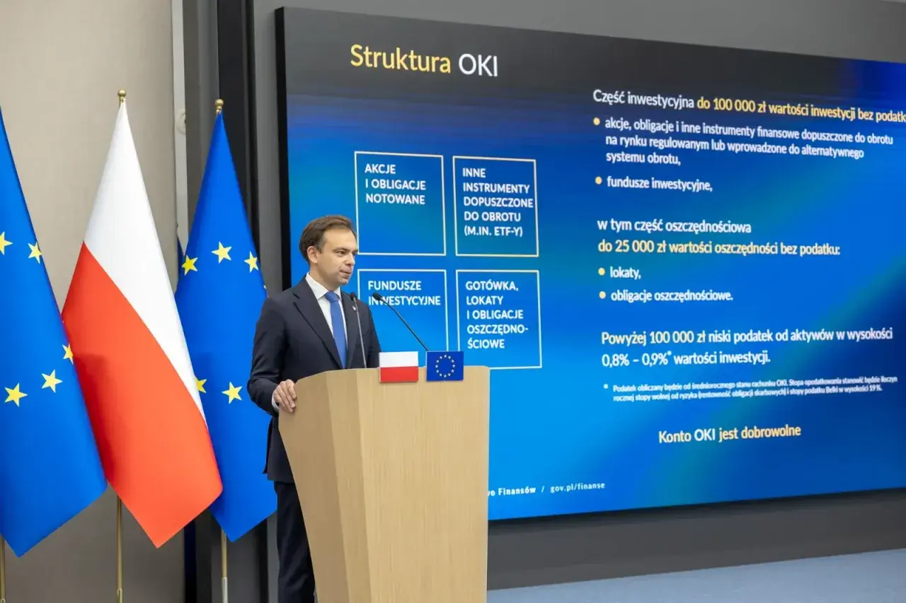 Mężczyzna przemawia przy mównicy, obok flagi Polski i UE. Na ekranie struktura OKI, inwestycje, lokaty, obligacje oszczędnościowe, rachunek oszczędnościowy plus opłaty.