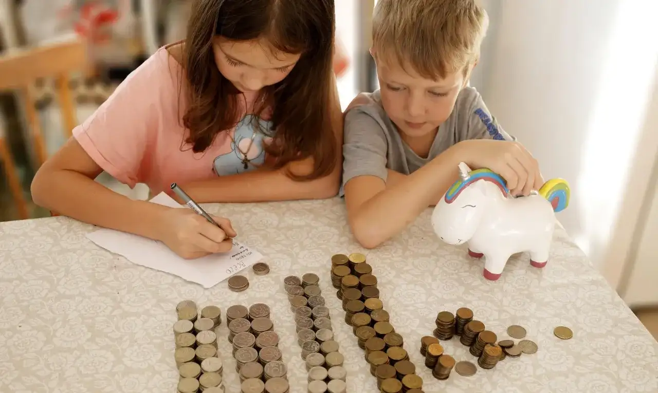 Dzieci liczą monety przy skarbonce w kształcie jednorożca. To świetny sposób na naukę oszczędzania, jak na nest bank konto dla dziecka.