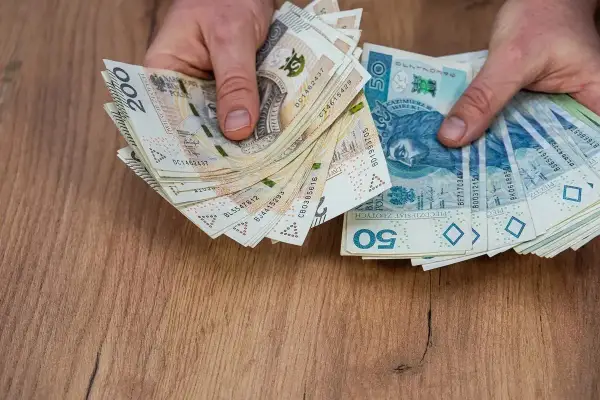 Dłonie trzymające stos polskich banknotów 50 zł i 200 zł na drewnianym tle.