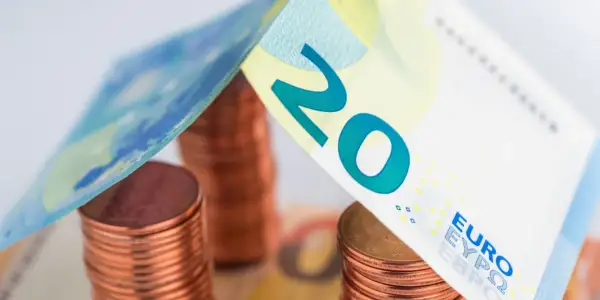 Stos monet euro i banknot 20 euro tworzą symboliczny dach nad domem.