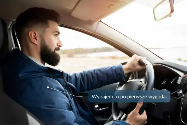 Mężczyzna z brodą prowadzi samochód, trzymając kierownicę.