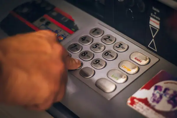 Dłoń wpisująca PIN na klawiaturze bankomatu.