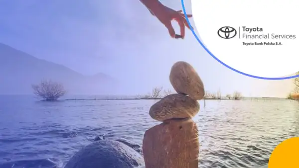 Równowaga kamieni na brzegu jeziora, ręka kładzie ostatni kamień. Logo Toyota Bank.
