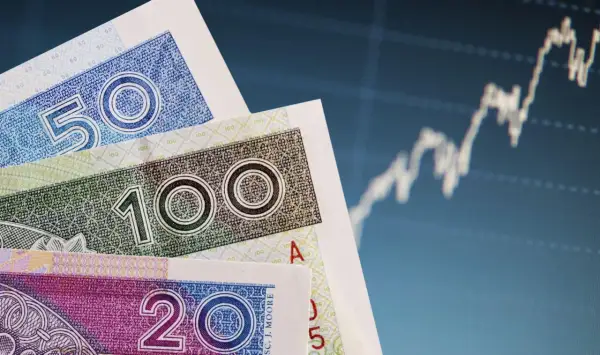 Polskie banknoty 50, 100 i 200 zł na tle wykresu giełdowego.