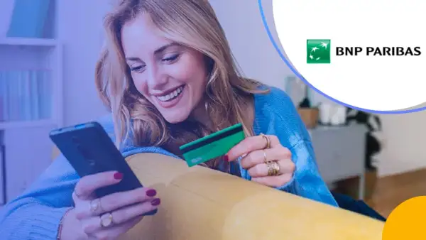 Uśmiechnięta kobieta z kartą płatniczą BNP Paribas w ręku korzysta z telefonu. Sprawdza BNP Paribas opłaty i prowizje.