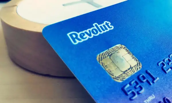Niebieska karta Revolut z chipem i częścią numeru, na tle drewnianego przedmiotu.